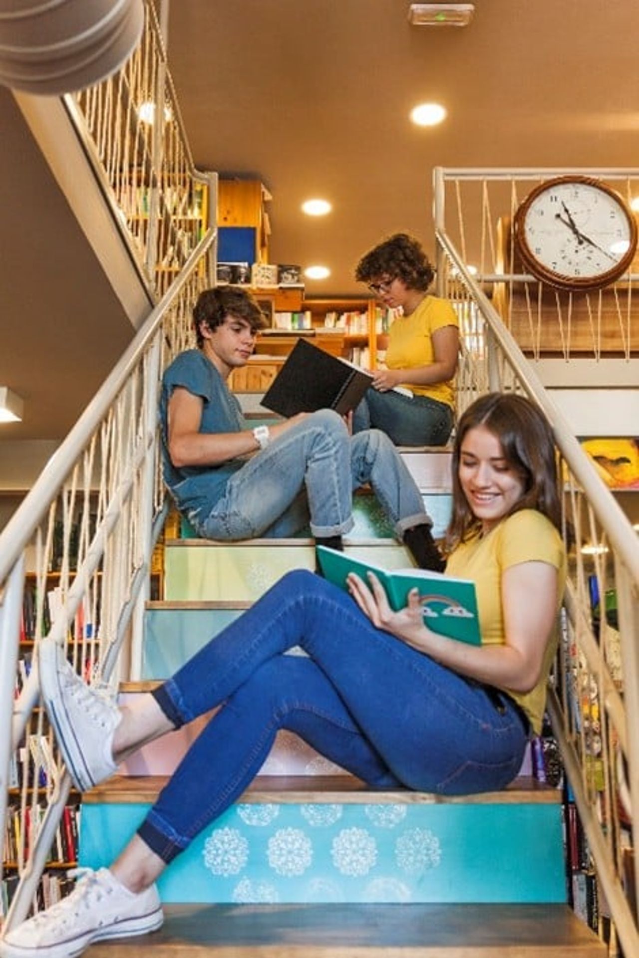 Tre ungdomar sitter i en trappa och läser böcker